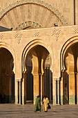 Marokko,Zwei Männer gehen in der Abenddämmerung über den Hof vor der Hassan-II-Moschee,Casablanca