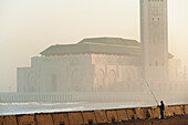 Morocco,Man fishing from sea wall in front of Hassan II mosque at dawn,Casablanca