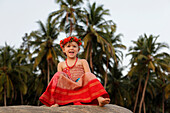 A girl on a rock in a red dress with flowers in her hair,Patnum beach,Goa,India.