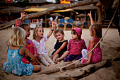 Mädchen plaudern im Schatten eines traditionellen Fischerboots vor einem Strandrestaurant, Patnum Beach, Goa, Indien.