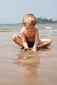 A boy plays with sand on Patnum beach,Goa,India.