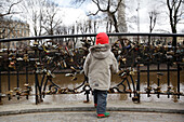 Ein kleiner Junge spielt mit den Schlössern, die an der Love Lock Bridge im Baste Kalns Park befestigt sind. Es bringt Glück und ist Tradition, dass die Bräutigame ihre Bräute über die 7 Brücken in Riga tragen und ihr Schloss anbringen, um ihre Liebe zu besiegeln,Riga,Lettland.