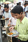 Locals eat plate-meal while standing up at this cheap on-street cafe in centre of Calcutta / Kolkata,the capital of West Bengal State,India,Asia.