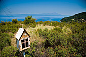 Greece,Halkidiki,Rusty miniature church roadside shrine with Mount Athos in distance,Sithonia