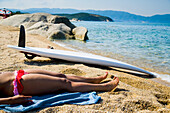 Greece,Halkidiki,Young woman sunbathing on beach with surf board on sand,Ierissos