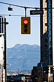 Ampel, die an einem Kabel zwischen Gebäuden aufgehängt ist, mit Blick auf einen Berg im Hintergrund, Vancouver, British Columbia, Kanada