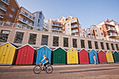 Radfahrer, Fußgänger, farbenfrohe Strandhütten und Apartments in der Honeycombe-Beach-Siedlung neben dem Boscombe Pier, Bournemouth, Dorset, England, Großbritannien