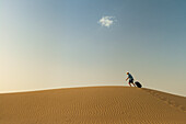 Barefoot Man With Suitcase Walking On Sand Dune,Dubai,United Arab Emirates