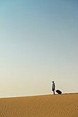 Barfüßiger Mann mit Koffer auf Sanddüne,Dubai,Vereinigte Arabische Emirate