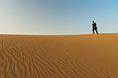 Mann im eleganten Anzug geht in der Abenddämmerung auf einer Sanddüne spazieren, Dubai, Vereinigte Arabische Emirate