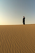 Mann im schicken Anzug telefoniert in der Dämmerung auf einer Sanddüne, Dubai, Vereinigte Arabische Emirate
