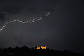 Blitzeinschlag in den dunklen Himmel und ein beleuchtetes Schloss darunter,Bellinzona,Tessin,Schweiz