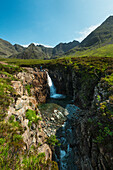 Mann schaut auf einen kleinen Wasserfall und einen der Fairy Pools in Coire Na Creiche, Black Cuillin, Isle Of Skye, Schottland
