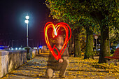 Ein Mann zeichnet eine rot leuchtende Herzform in die Luft, Locarno, Tessin, Schweiz