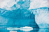 Nahaufnahme der zerklüfteten blauen Eiswände eines großen Eisbergs, der sich im Wasser spiegelt,Antarktis