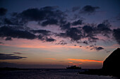 Silhouette eines Kreuzfahrtschiffes bei Sonnenuntergang in der Nähe der Insel San Cristobal im Nationalpark der Galapagos-Inseln, San Cristobal Island, Galapagos-Inseln, Ecuador