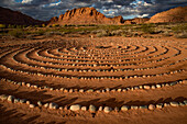 Hiking trail through Snow Canyon,with circles of stones in a meeting area behind the Red Mountain Spa,with meditation maze and Snow Canyon Mountain Range in the background. Red Cliffs Desert Reserve around St George Town with rock cliffs and dark clouds in a blue sky,St George,Utah,United States of America