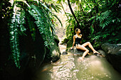 Woman relaxing on the rocks surrounding the hot springs at Trafalgar Falls enjoying the atmosphere of the lush rainforest on the Caribbean Island of Dominica in Morne Trois Pitons National Park,Dominica,Caribbean