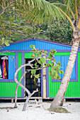 Nahaufnahme einer farbenfrohen Strandhütten-Boutique am Sandstrand von Cane Garden Bay mit Palmen und tropischen Pflanzen, Tortola, Britische Jungferninseln, Karibik