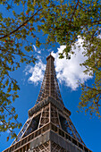 Niedriger Winkel des Eiffelturms vor einem blauen Himmel mit Wolken, umgeben von Baumzweigen, Paris, Frankreich