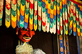Mask displayed in a farmhouse behind hanging colorful decorative fabric,Paro Valley,Bhutan