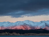 Das Licht der Morgendämmerung beleuchtet die verschneiten Rhoboro Hills mit dem ruhigen Lake Pukaki im Vordergrund, Twizel, Südinsel, Neuseeland
