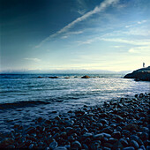 Person stands on a rocky slope looking out to the water along the tranquil coast,Alaska,United States of America