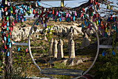 Blick durch einen kreisförmigen Schaukelsitz, der mit bunt bemalten Keramikvasen verziert ist, auf die Feenkamin-Felsformationen im Liebestal nahe der Stadt Goreme, Region Kappadokien, Provinz Nevsehir, Türkei