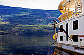 Ein Mann genießt seinen Urlaub mit der Familie auf einem Hausboot und angelt vom Deck des Hausbootes aus, während es am Ufer des Shuswap Lake, Shuswap Lake, British Columbia, Kanada, geparkt ist