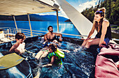 Eine Gruppe von Familienmitgliedern, die einen Hausbooturlaub genießen, während sie am Ufer des Shuswap Lake parken und im Whirlpool auf dem Boot sitzen, Shuswap Lake, British Columbia, Kanada