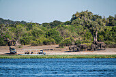 Touristen, die auf einer Safari im Chobe-Nationalpark Elefanten vom Fluss und vom Land aus beobachten, Botswana