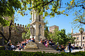 School children having a lunch break,monument to the Immaculate Conception,Plaza del Triunfo,Real Alcazar in background,Seville,Andalusia,Spain