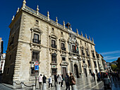 Fußgänger, die an einem Gebäude auf der Plaza Neuva bei strahlend blauem Himmel vorbeigehen, Granada, Andalusien, Spanien