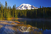 Snow-covered Mount Rainier at sunrise,with frosty vegetation on the shore and mist rising up from the water of Reflection Lake,Washington,United States of America