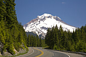Highway schlängelt sich durch den Wald mit Blick auf den verschneiten Mount Hood, Mount Hood National Forest, Oregon, Vereinigte Staaten von Amerika