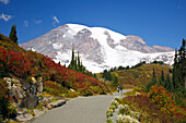 Zwei Wanderer auf einem Pfad im Mount Rainier National Park mit dem verschneiten und majestätischen Mount Rainier im Hintergrund, Washington, Vereinigte Staaten von Amerika