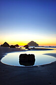 Silhouettierte Felsformationen am Bandon Beach bei Sonnenuntergang und Ebbe, Oregon-Küste, Oregon, Vereinigte Staaten von Amerika