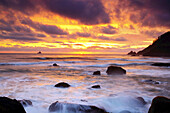 Warmes Sonnenuntergangslicht, das in den Wolken über der Küste von Oregon mit ruhigem Wasser und zerklüfteten Felsen und dem Horizont in der Ferne glüht, Oregon, Vereinigte Staaten von Amerika