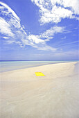 A bright yellow beach towel lays on a patch of white sand surrounded by turquoise ocean water in the Maldives,Maldive Islands,Republic of Maldives