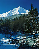 Snow-covered Mount Hood against a bright blue sky and a river flowing through Mount Hood National Forest,Oregon,United States of America