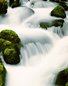 Bewegungsunschärfe von kaskadierendem Wasser, das über moosbewachsene Felsen fließt, Oregon, Vereinigte Staaten von Amerika