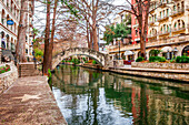 Gewölbte Fußgängerbrücke über den ruhigen San Antonio River auf dem San Antonio River Walk, San Antonio, Texas, Vereinigte Staaten von Amerika