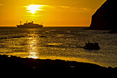 Ein Schlauchboot und die National Geographic Endeavour bei Sonnenuntergang.