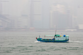 A boat crosses the harbor in front of a foggy Hong Kong.