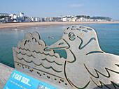 View of seashore from pier with metal plaque shaped as seagull and waves,Hastings,East Sussex,England