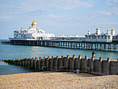 Blick auf den Pier mit goldener Kuppel, ruhiger See, blauem Himmel und Kieselstrand,Eastbourne,East Sussex,England