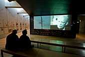 Touristen betrachten eine Filmvorführung im Museum des Soldatenfriedhofs in der Normandie, Coleville-sur-Mer, Normandie, Frankreich