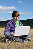 Boy Sitting in Field using Laptop Computer,Blandas,Gard,France