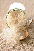 Nahaufnahme von Reis, der mit einem Holzlöffel aus einem Glasgefäß verschüttet wird
