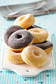Nahaufnahme von Donuts mit Zuckerüberzug und Schokoladenüberzug auf Schneidebrett vor blauem Hintergrund